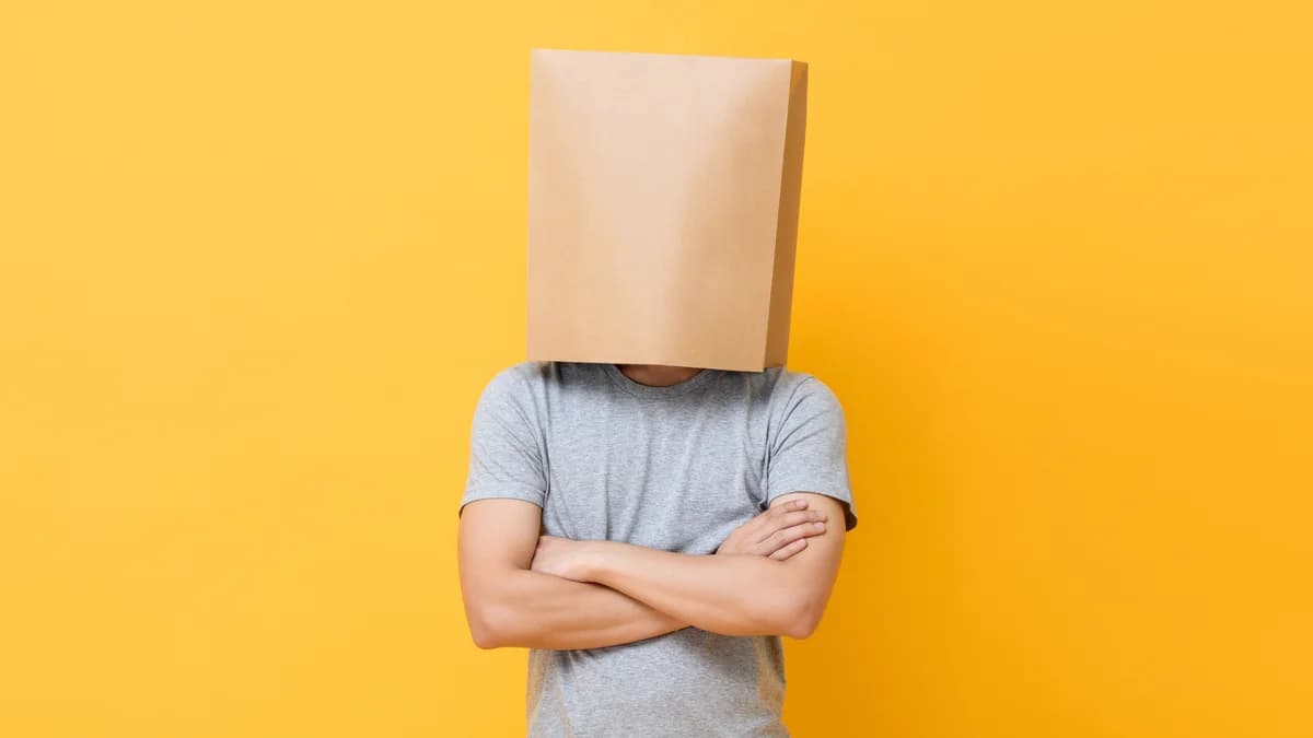 Concept portrait of Anonymous man with head covered with paper bag doing arms crossed gesture in yellow studio background